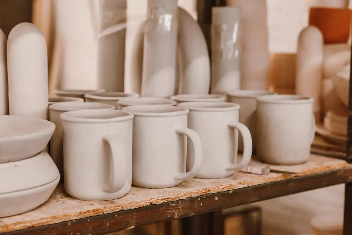 Tasses et pièces de céramique blanche non émaillées, alignées sur une étagère