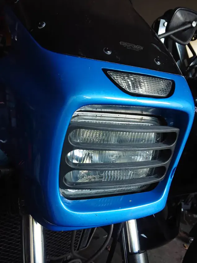 Grille de protection de phare imprimée en 3D, montée sur le carénage bleu d’une moto