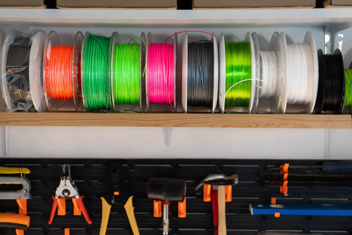 Bobines de filament pour impression 3D rangées sur une étagère, au-dessus d’un panneau d’outils