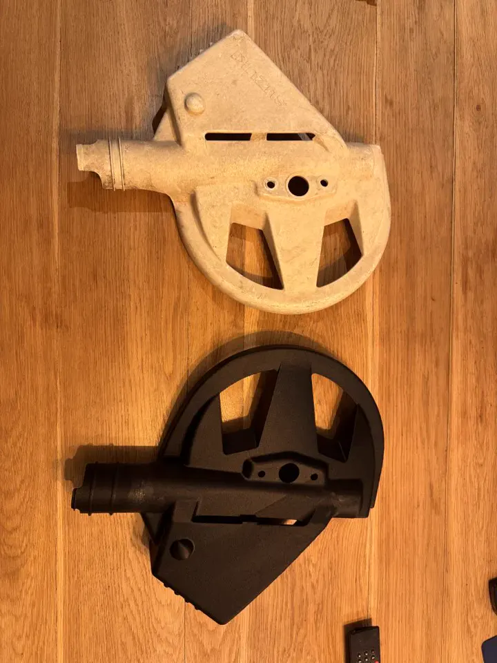 Une pièce d’origine claire et cassée, et sa copie noire imprimée en 3D, posées sur une planche de bois