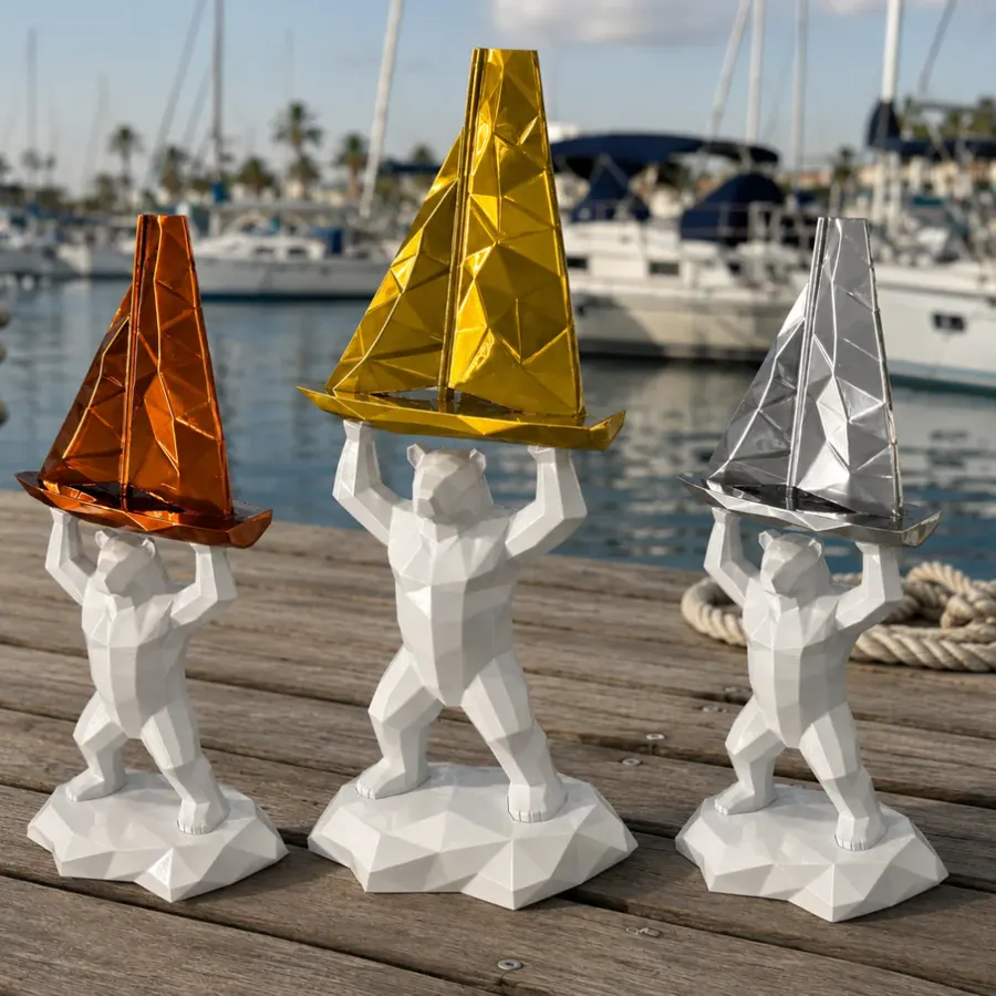 Les trois trophées de la Vendée Arctique 2026 sur un ponton : ours blancs à facettes portant un voilier bronze, or et argent